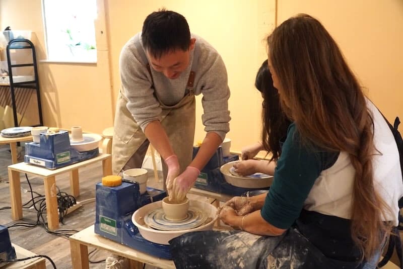 Guiding a student's hands as they center clay on the pottery wheel at our studio.